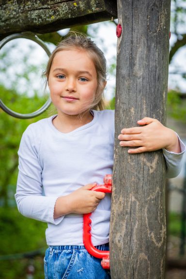 Ein Mädchen mit langen, braunen Haaren steht an einem Spielplatzspielgerät.