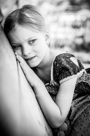 Ein Mädchen in einem Kleid lehnt nachdenklich an einer Wand, mit melancholischem Ausdruck.