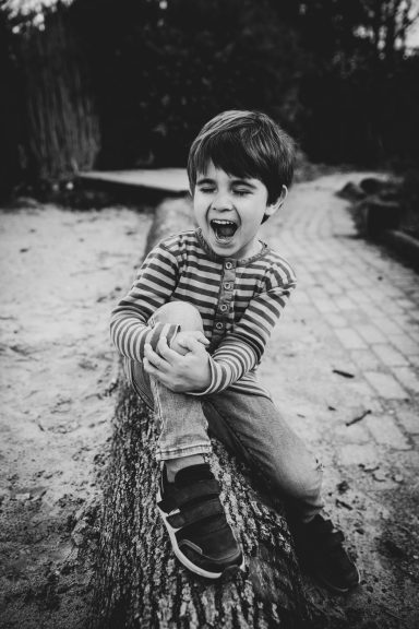 Ein Junge sitzt auf einem Baumstamm und lacht fröhlich.