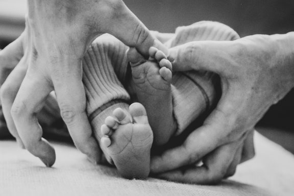 Zwei Hände halten die Füße eines Babys, sanft und liebevoll.