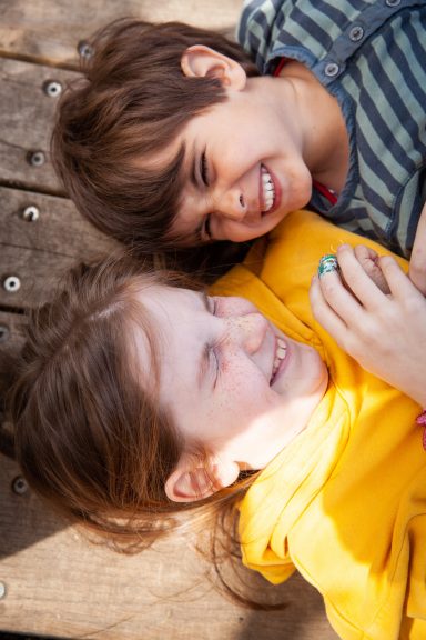 Zwei Kinder liegen lachend auf dem Boden und haben viel Spaß zusammen.