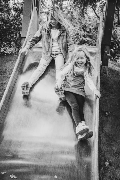 Zwei Kinder rutschen fröhlich eine Rutsche hinunter in einem Garten.