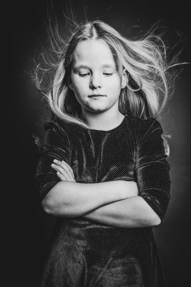 Ein Mädchen mit langen, fließenden Haaren, die Arme verschränkt und mit geschlossenen Augen.