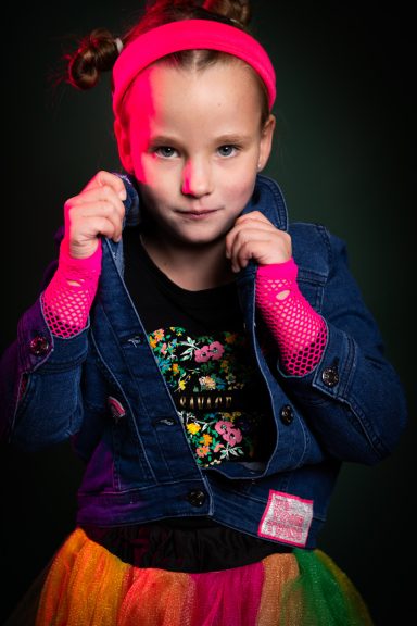 Ein Mädchen mit Zopf, Jeansjacke und buntem Rock posiert selbstbewusst.