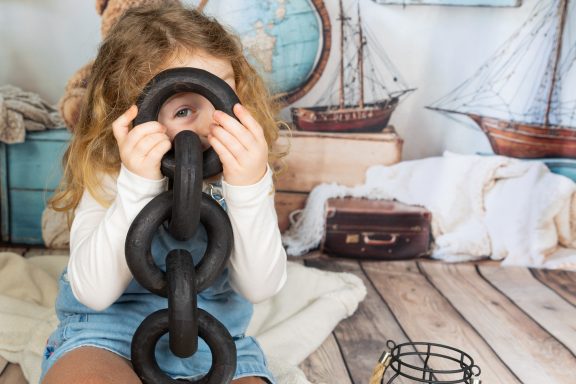 Ein Mädchen hält eine Kette und schaut durch einen der Ringe, mit maritimem Hintergrund.