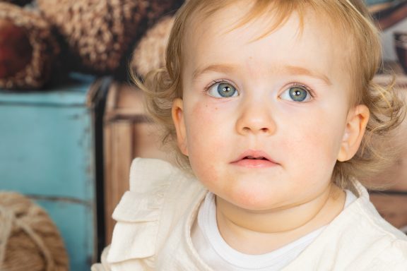Kleines Kind mit blonden lockigen Haaren und blauen Augen, schaut nachdenklich.