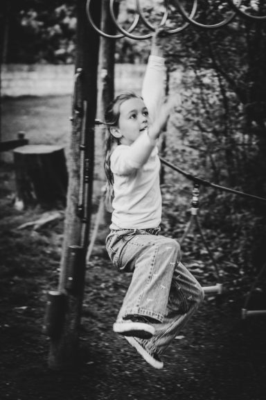 Ein Kind schwingt an einer Spielplatzstange in einem Park.