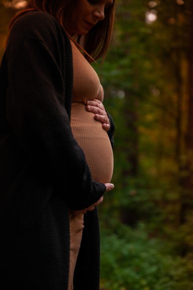Schwangere Frau in einem grünen Wald, die sanft ihren Bauch hält.