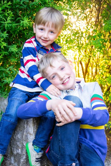 Zwei fröhliche Jungen posieren lächelnd auf einem Baumstamm im Freien.