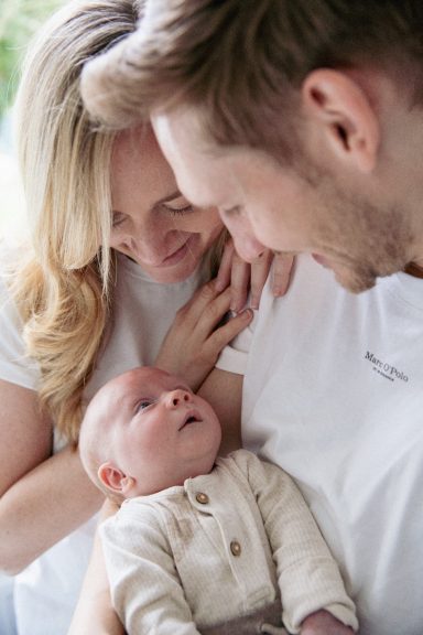Ein lächelndes Paar hält ihr Neugeborenes in liebevoller Umarmung.