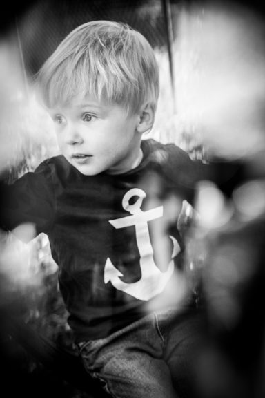 Ein kleiner Junge mit blonden Haaren sitzt inmitten von Blumen und trägt ein Shirt mit Anker.