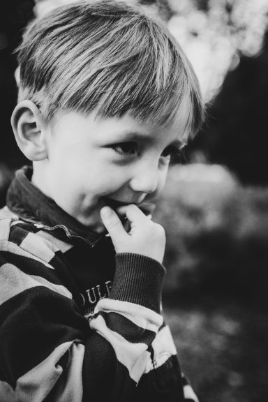 Ein Junge mit blonden Haaren, der nachdenklich wirkt und an seinem Finger kaut.