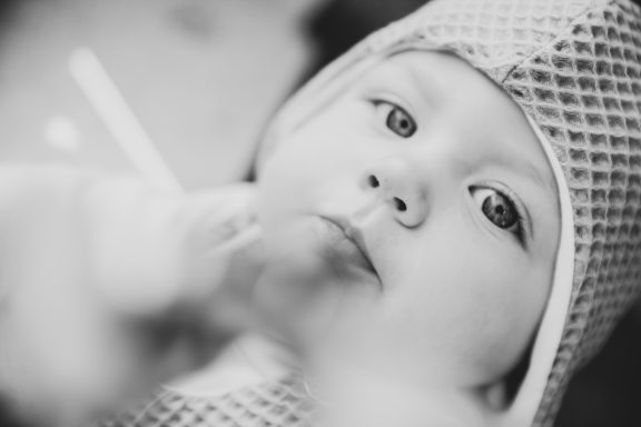 Ein Baby mit großen Augen in einem Mützchen schaut neugierig.