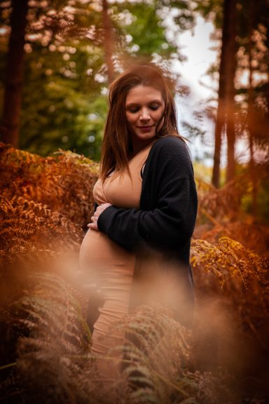 Schwangere Frau in einem Wald mit herbstlichen Farben, umgeben von hohen Pflanzen.