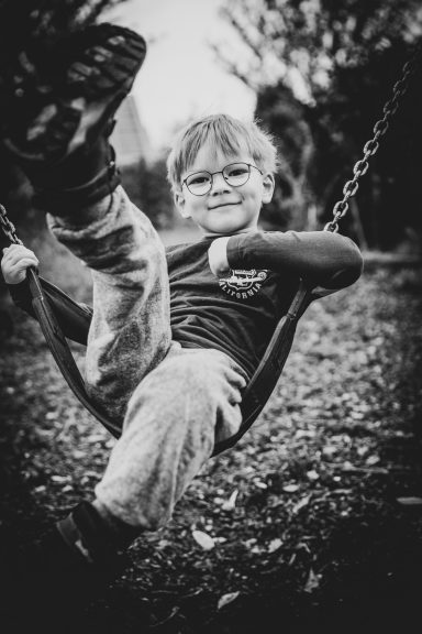 Junge schwingt fröhlich auf einer Schaukel im Freien, lächelnd und entspannt.