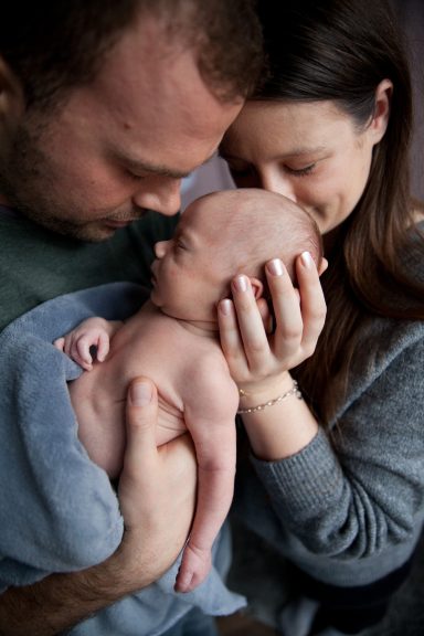 Neugeborenes Baby wird liebevoll von Eltern umarmt und bevorsichtigt.