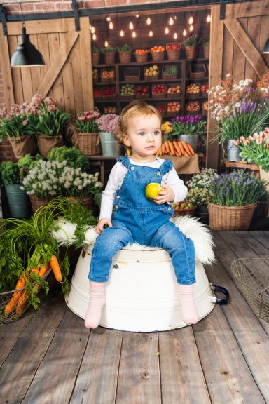 Ein kleines Mädchen mit einem gelben Apfel sitzt in einem Blumenladen.