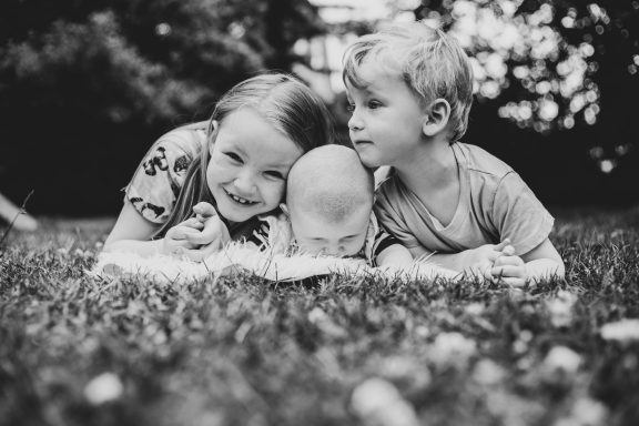 Drei Kinder liegen lächelnd auf dem Gras und genießen die gemeinsame Zeit.