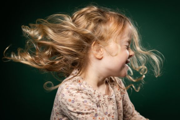 Ein fröhliches Mädchen mit lockigem, schwingendem Haar auf grünem Hintergrund.