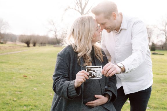 Schwangere Frau und Mann halten ein Ultraschallbild lachend im Park.