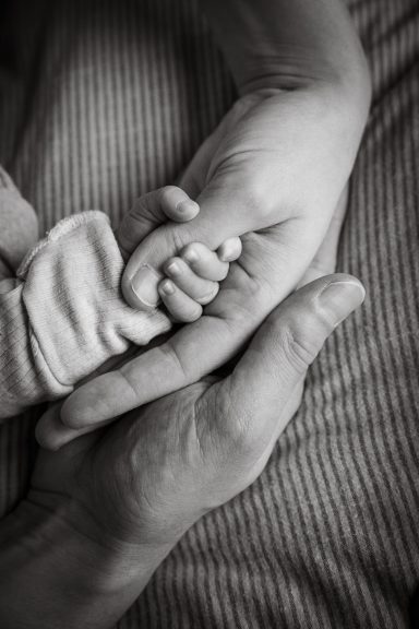 Hände eines Erwachsenen halten die kleine Hand eines Babys liebevoll.