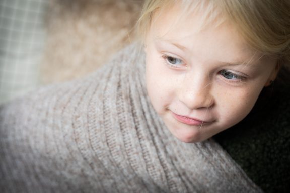 Ein kleines Mädchen eingewickelt in eine Decke, schaut nachdenklich zur Seite.