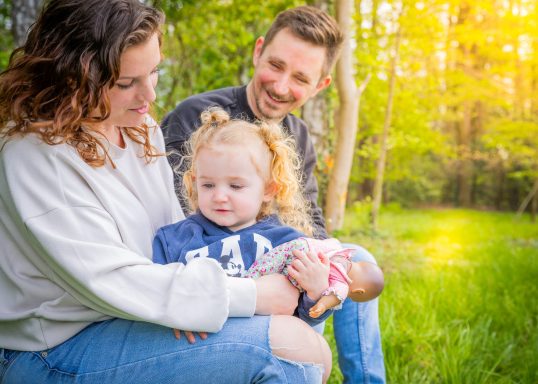 Eine Familie sitzt im Freien, ein Paar und ein kleines Mädchen auf dem Schoß der Mutter.