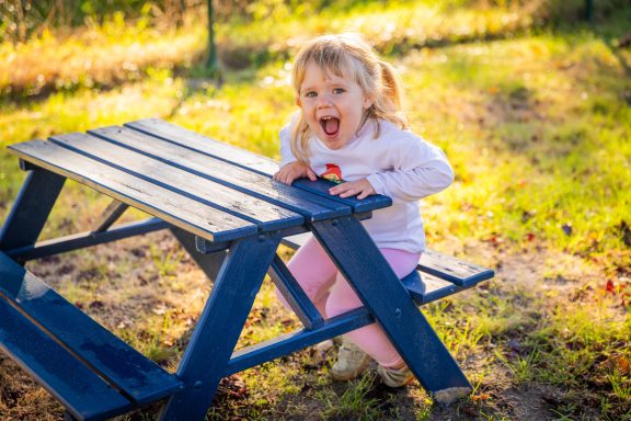 Ein fröhliches Kind sitzt auf einer blauen Picknickbank im Freien.