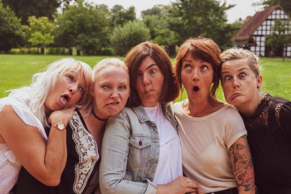 Fünf Frauen posieren humorvoll mit grimmigen Gesichtsausdrücken im Freien.