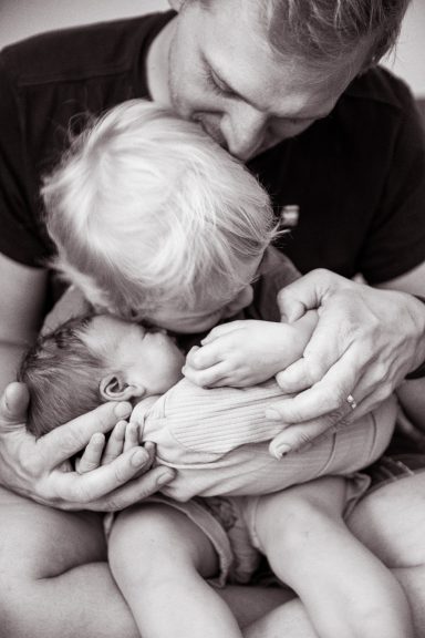 Ein Vater umarmt seine beiden Kinder liebevoll auf seinem Schoß.