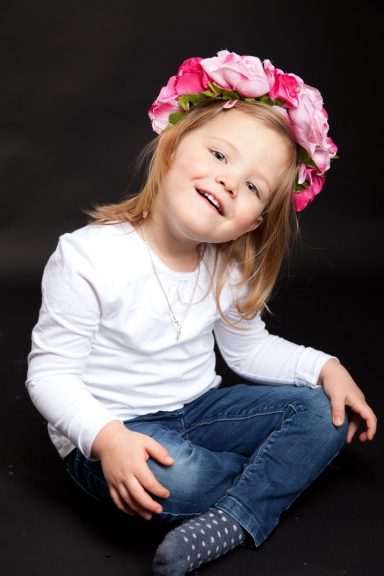 Ein lächelndes Mädchen mit Blumenkranz sitzt in einer lässigen Pose.