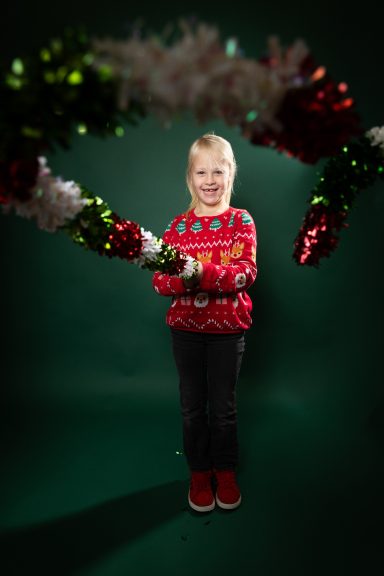 Ein lächelndes Kind in einem festlichen Pullover hält glitzernde Dekorationen.