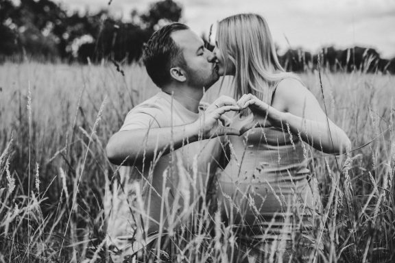 Paar küsst sich im Feld, während sie mit den Händen ein Herz formen.