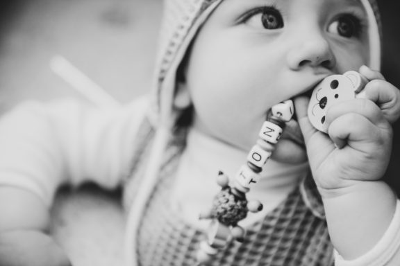 Ein kleines Kind mit Schnuller und Spielzeugbuchstaben in schwarz-weiß.