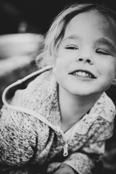 Lächelndes Kind mit blonden Haaren in einem hellen Sweatshirt.