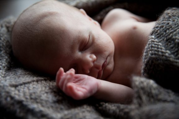 Schlafendes Baby mit kurzem Haar, eingehüllt in eine graue Decke.