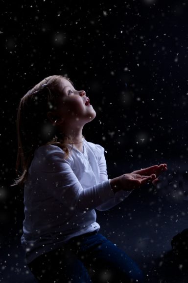 Ein Kind schaut nach oben und fängt Schneeflocken mit offenen Händen.