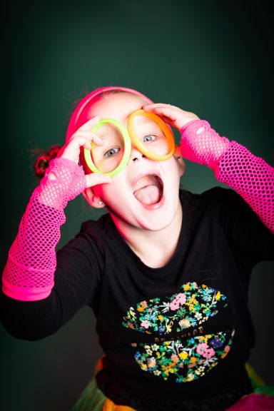 Ein fröhliches Mädchen trägt bunte Brillen und posiert spielerisch.