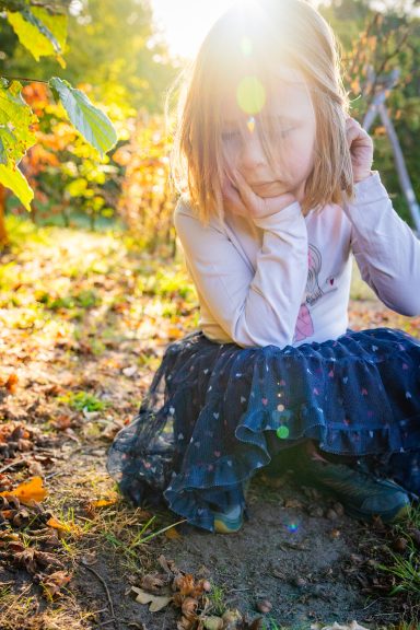 Mädchen in einem pinken Oberteil und blauer Tüllröcke sitzt nachdenklich im Freien.