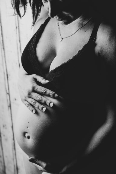 Schwangere Frau hält sanft ihren Bauch, in Schwarz-Weiß-Fotografie dargestellt.