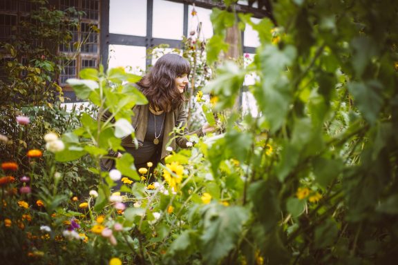 Person mit braunen Haaren zwischen bunten Blumen in einem Garten.