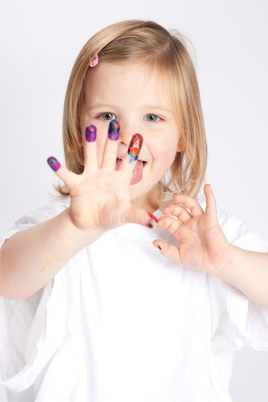 Ein kleines Mädchen zeigt stolz ihre bunt lackierten Nägel.