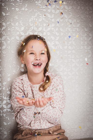 Ein lachendes Mädchen mit Konfetti, das fröhlich die Hände ausbreitet.