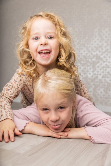 Zwei lächelnde Mädchen stehen und liegen auf einer Holzoberfläche.