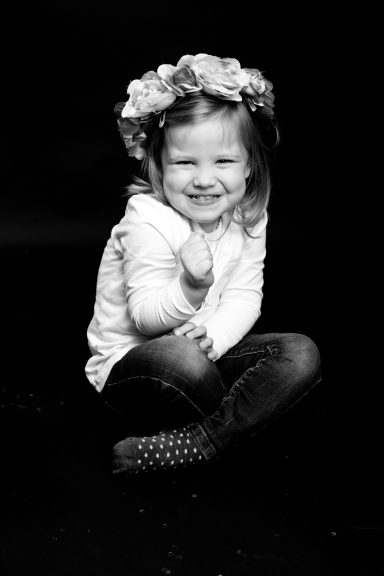 Lächelndes Kind mit Blumenkranz sitzt auf dem Boden und gibt Daumen hoch.