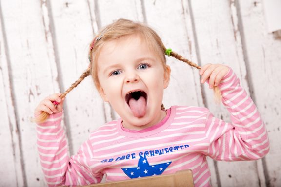 Lächelndes Mädchen mit Zöpfen, das die Zunge herausstreckt und Freude zeigt.