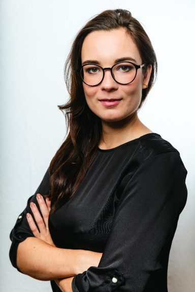 Junge Frau mit Brille und crossed arms, trägt ein schwarzes Oberteil.