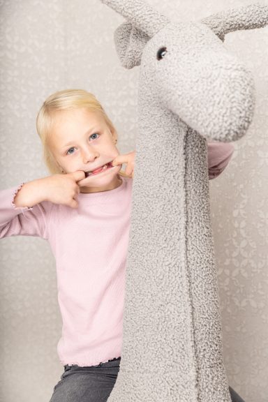 Ein Mädchen mit blonden Haaren macht Grimassen neben einem großen, grauen Stofftier.