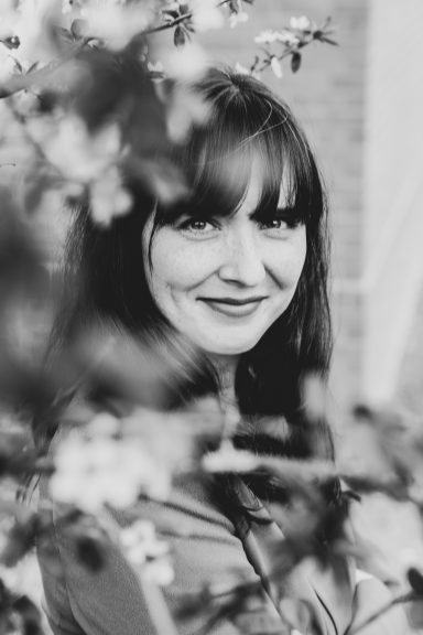 Porträt einer Frau mit langen Haaren, umgeben von blühenden Zweigen in Schwarzweiß.