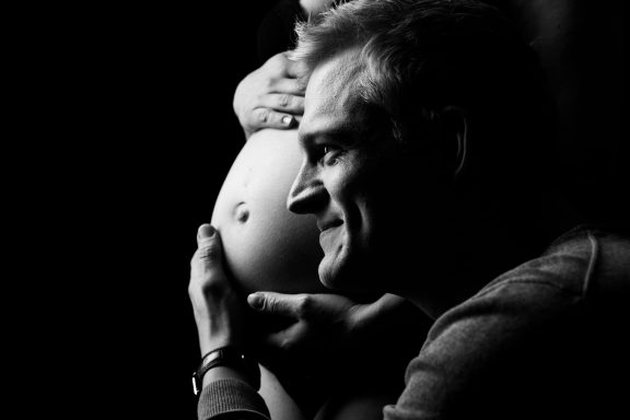 Vater lächelt verträumt, während er sanft einen schwangeren Bauch hält.